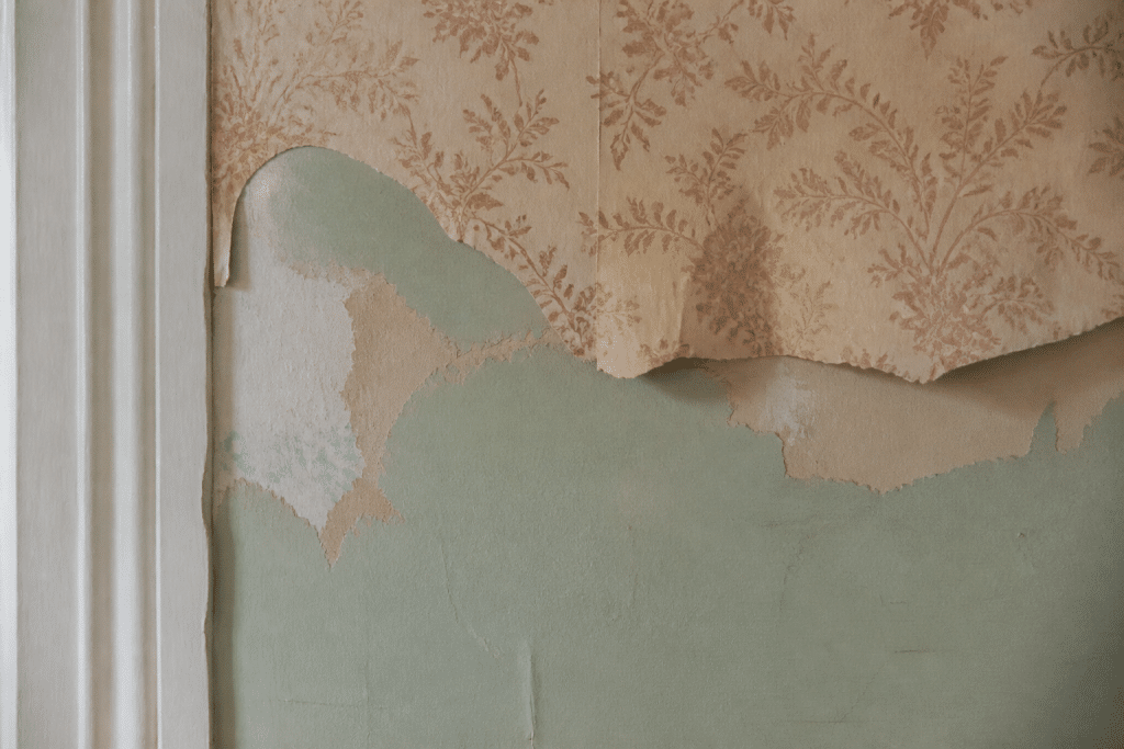 Mur avec papier peint ancien décollé révélant peinture