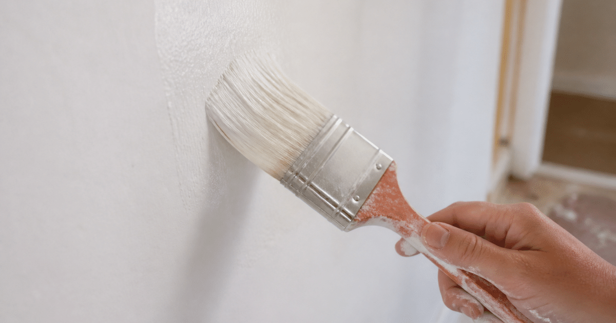 Pinceau appliquant peinture uniformement sur surface murale blanche