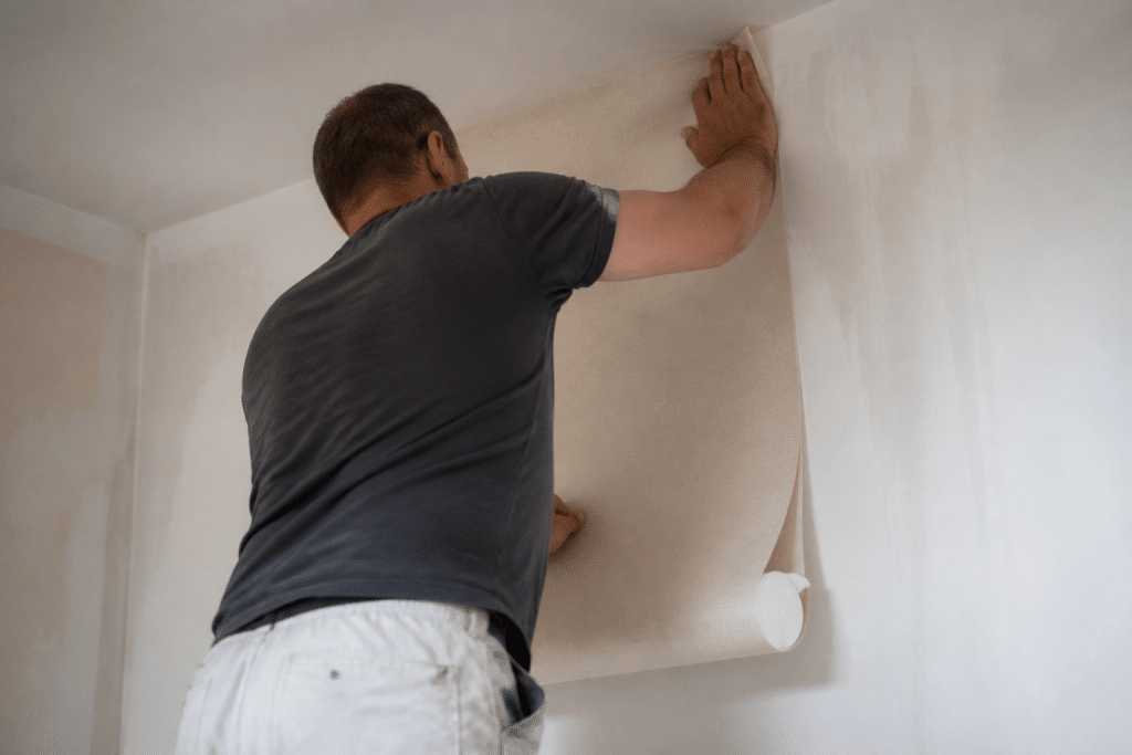 Ouvrier appliquant papier peint beige sur mur blanc préparé