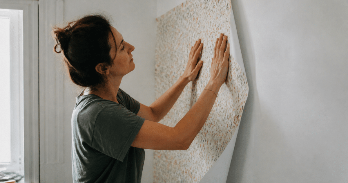 Personne collant feuille de papier peint sur mur blanc