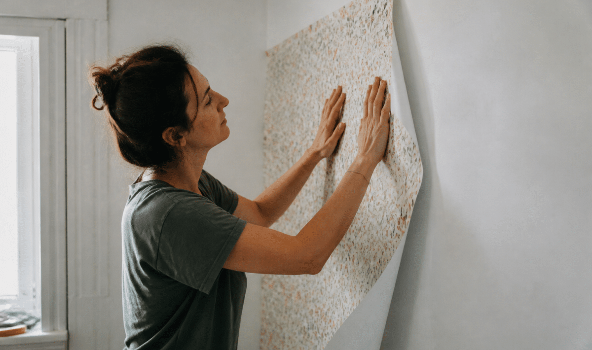 Personne collant feuille de papier peint sur mur blanc