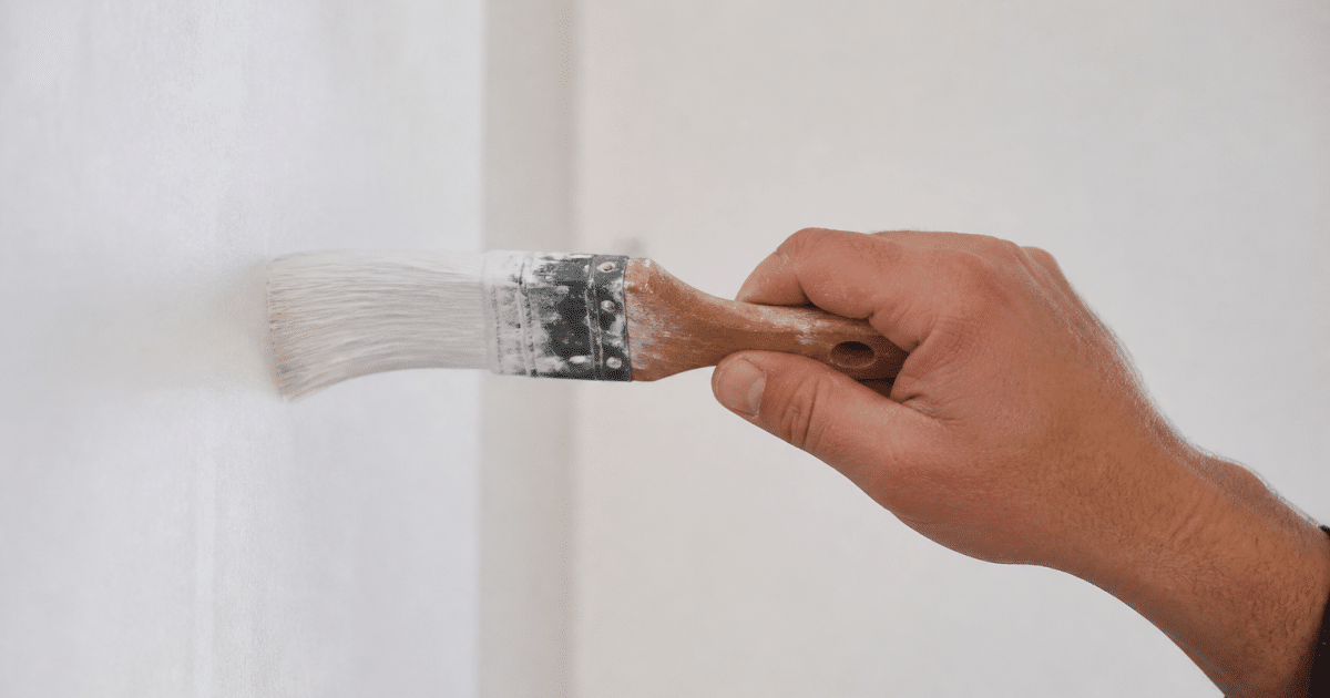 Pinceau applicateur tendu horizontalement contre surface murale blanche